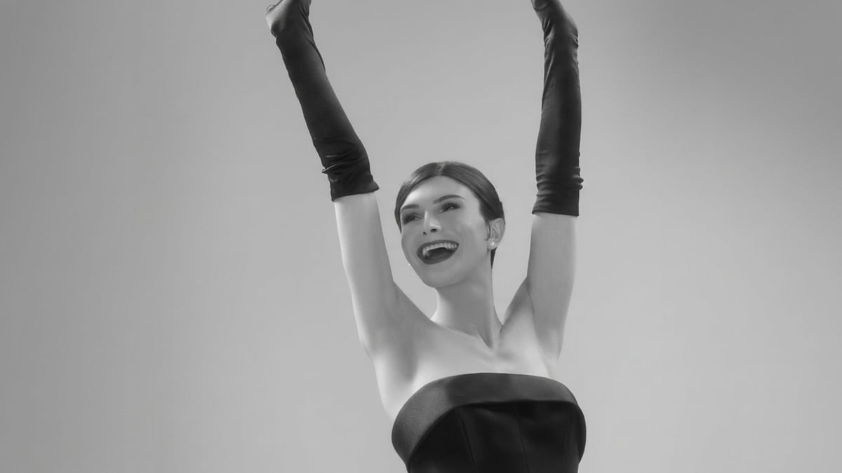 Influencer Dylan Mulvaney posing with arms up in a classic black strapless dress and opera gloves.
