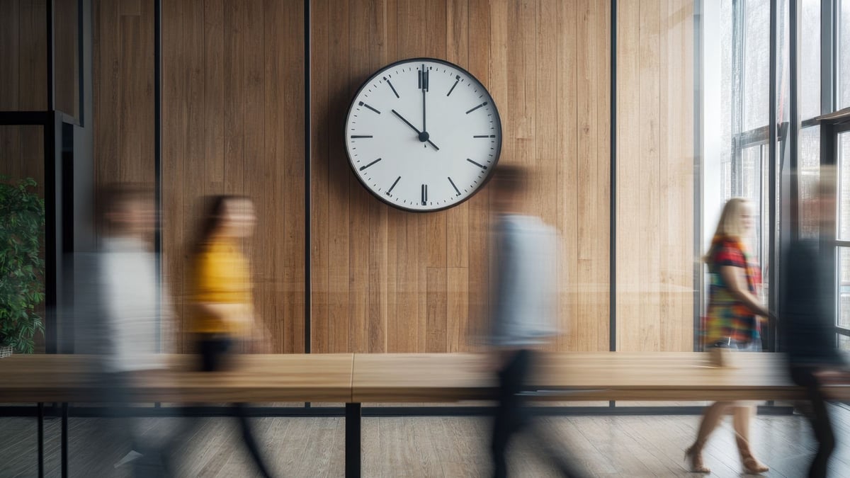 Blurred people passing by a clock on an office wall, showing the passing of time