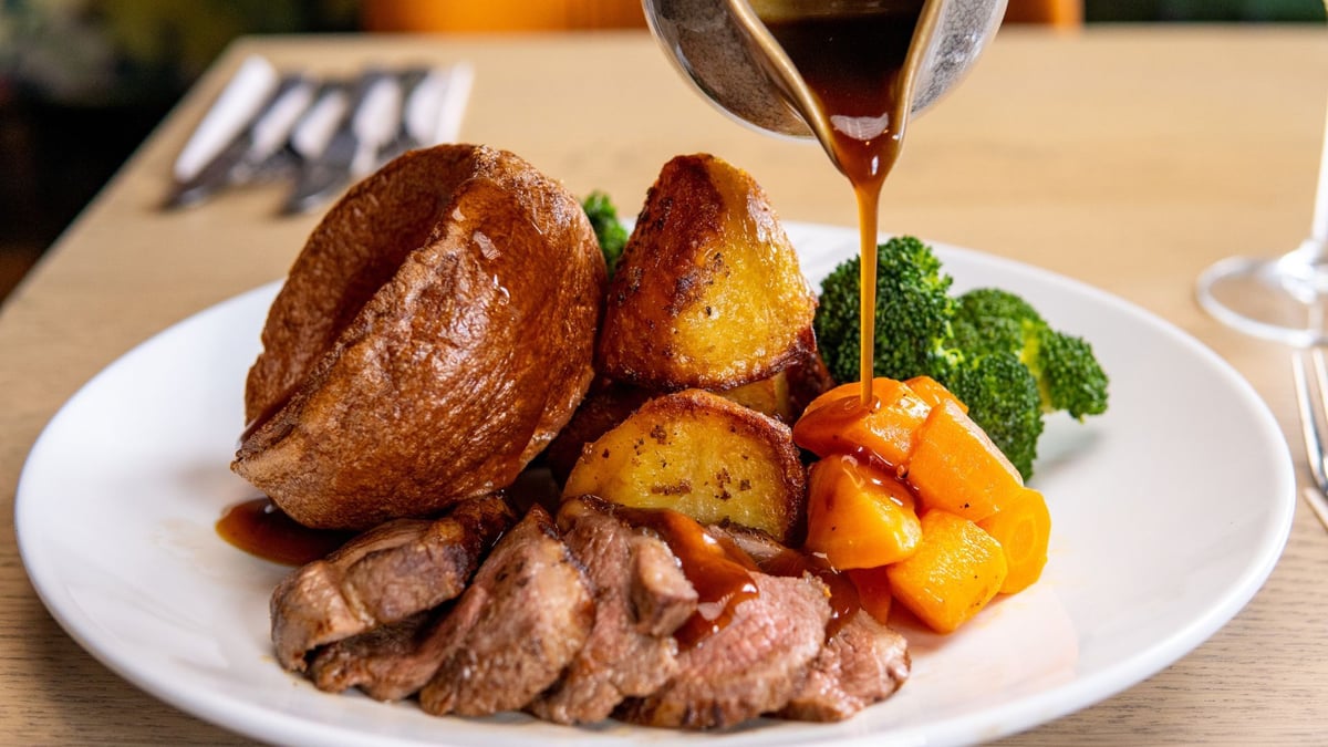 A traditional British roast dinner with meat, yorkshire puddings, potatoes, vegetables and gravy being poured on top